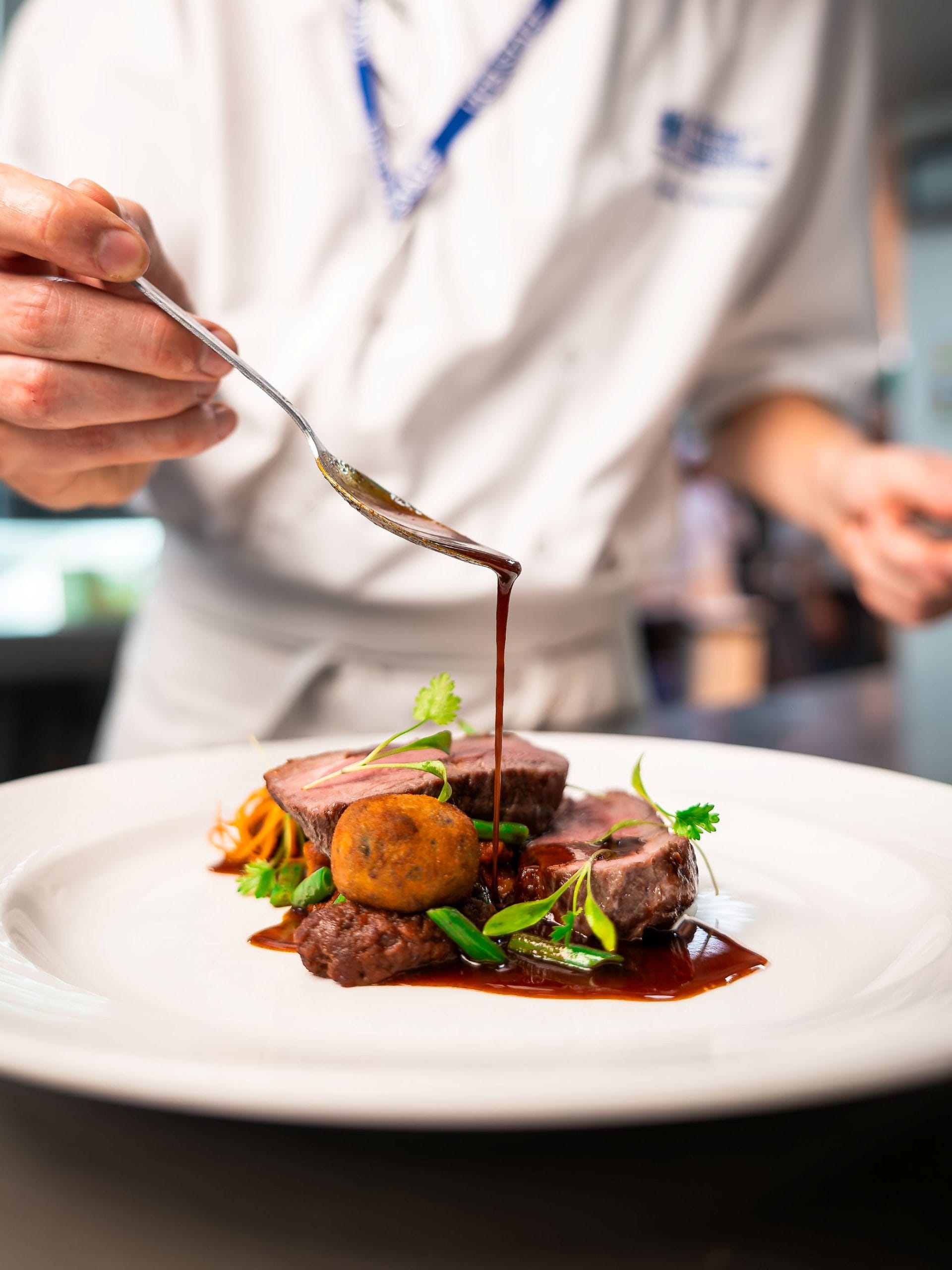 A person finishing off a dish by pouring gravy onto the dish via a spoon
