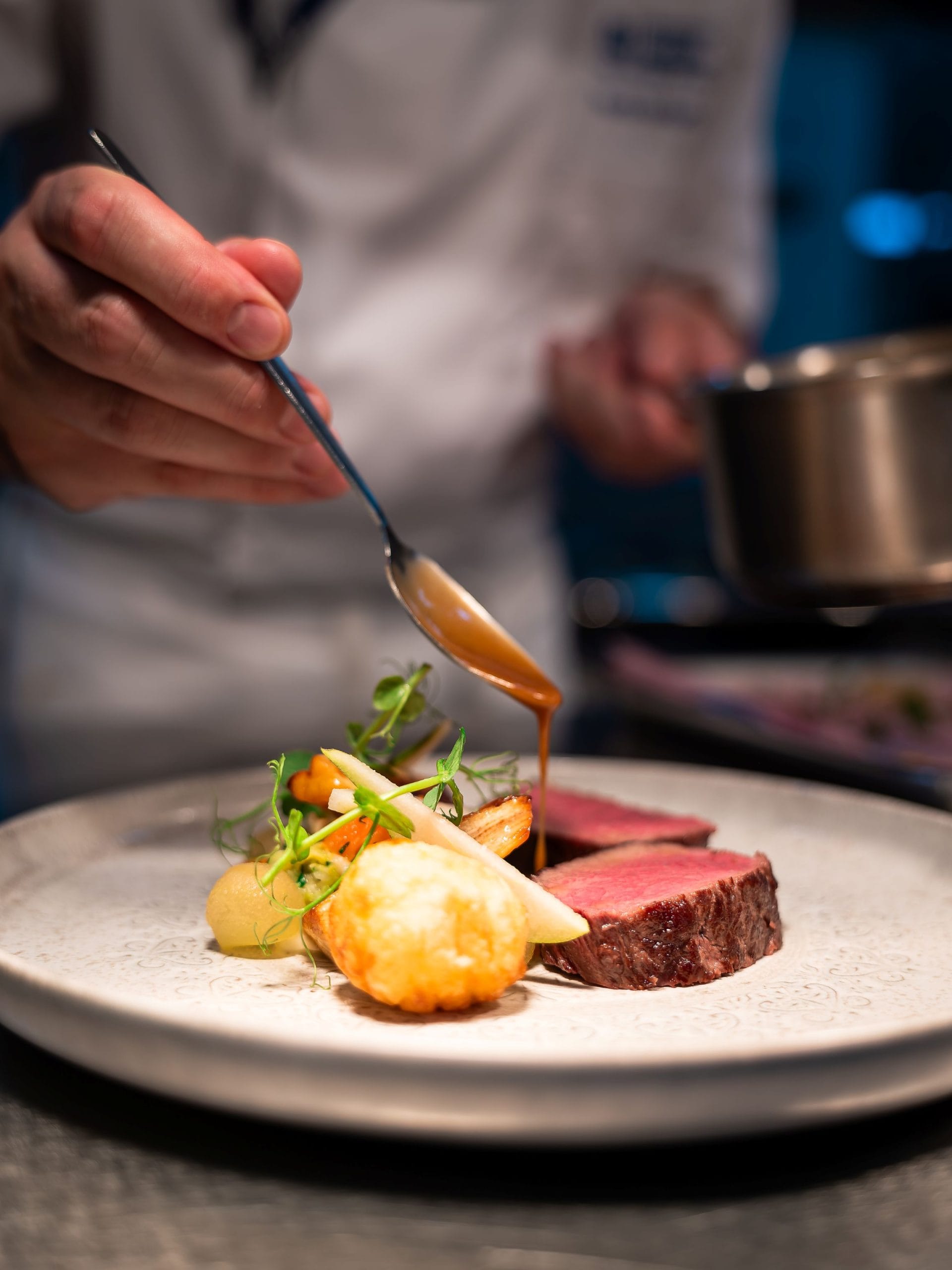 Plating a dish A hand holding a spoon which is drizzling gravy onto a dish